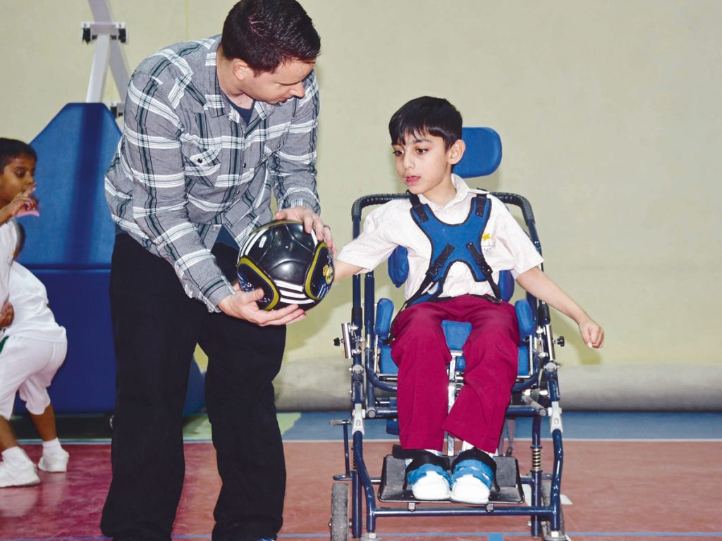 Where to volunteer in the UAE: Man holding football for young boy in wheelchair